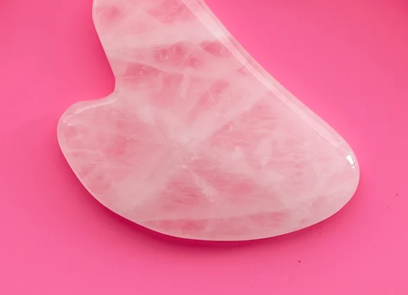 Rosa hjerteformet gua-sha-stein mot cerise bakgrunn.
