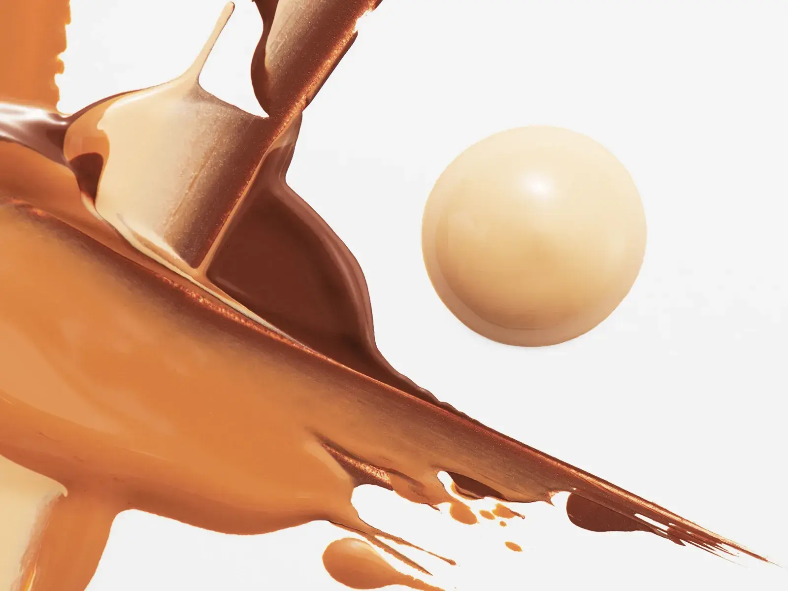 En concealer utspridd i ett abstrakt mönster i ljusbruna toner, med en rund klick concealer vid sidan – allt mot en vit bakgrund.