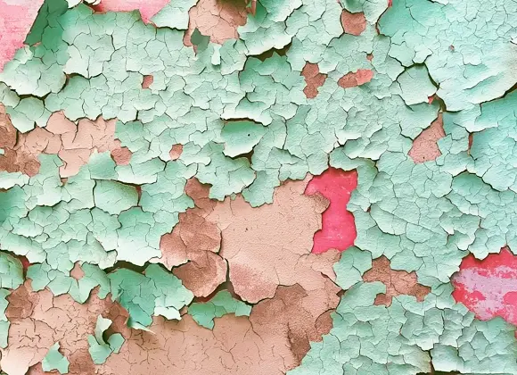 Närbild av en vägg med flagnande färg i turkosa, rosa och beige nyanser som avslöjar flera lager underliggande färg.