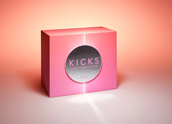 En rosa, lysande låda med Kicks-logga på framsidan, mot en bakgrund som tonas från vitt till orange.