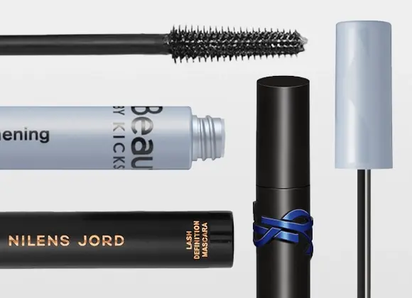 Useita ripsivärejä ja harjoja merkeiltä KICKS Beauty ja Nilens Jord, pakkauksissa tekstit "Beauty by KICKS" ja "NILENS JORD", mukana mustaa ripsivärimassaa ja avoimia pakkauksia vaalealla taustalla.