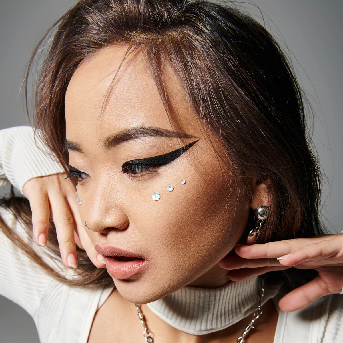 Kvinne med dramatisk eyeliner, rhinestone ansiktsperler og stilig tilbehør.