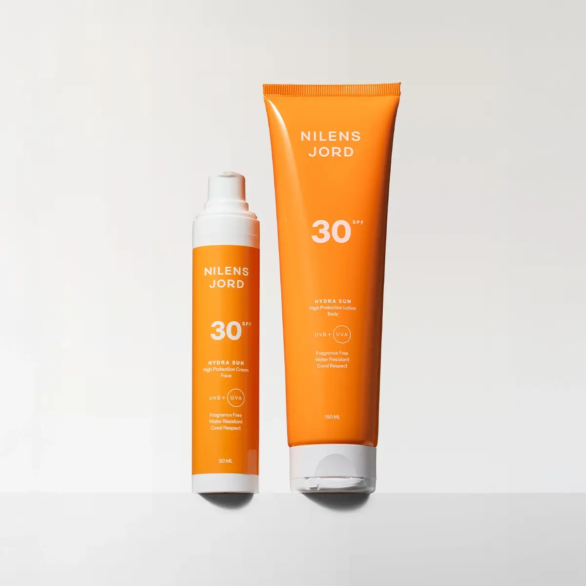 Två orange solskyddsprodukter från Nilens Jord Hydra Sun SPF 30 står mot en ljus bakgrund. Förpackningarna visar texten “Nilens Jord”, “30 SPF”, “Hydra Sun”, “High Protection Cream”, “High Protection Lotion Body”, “UVB + UVA”, “Fragrance Free”, “Water Resistant”, “Coral Respect”, samt storlekarna 50 ML och 150 ML.