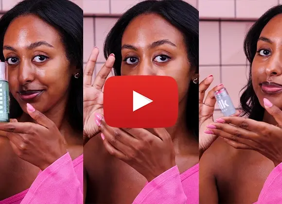 Henkilö, jolla on tummat hiukset ja vaaleanpunainen paita, levittää meikkiä ja näyttää Milk Makeup -tuotteen. Youtube play-merkki on sijoitettu kuvan keskelle.