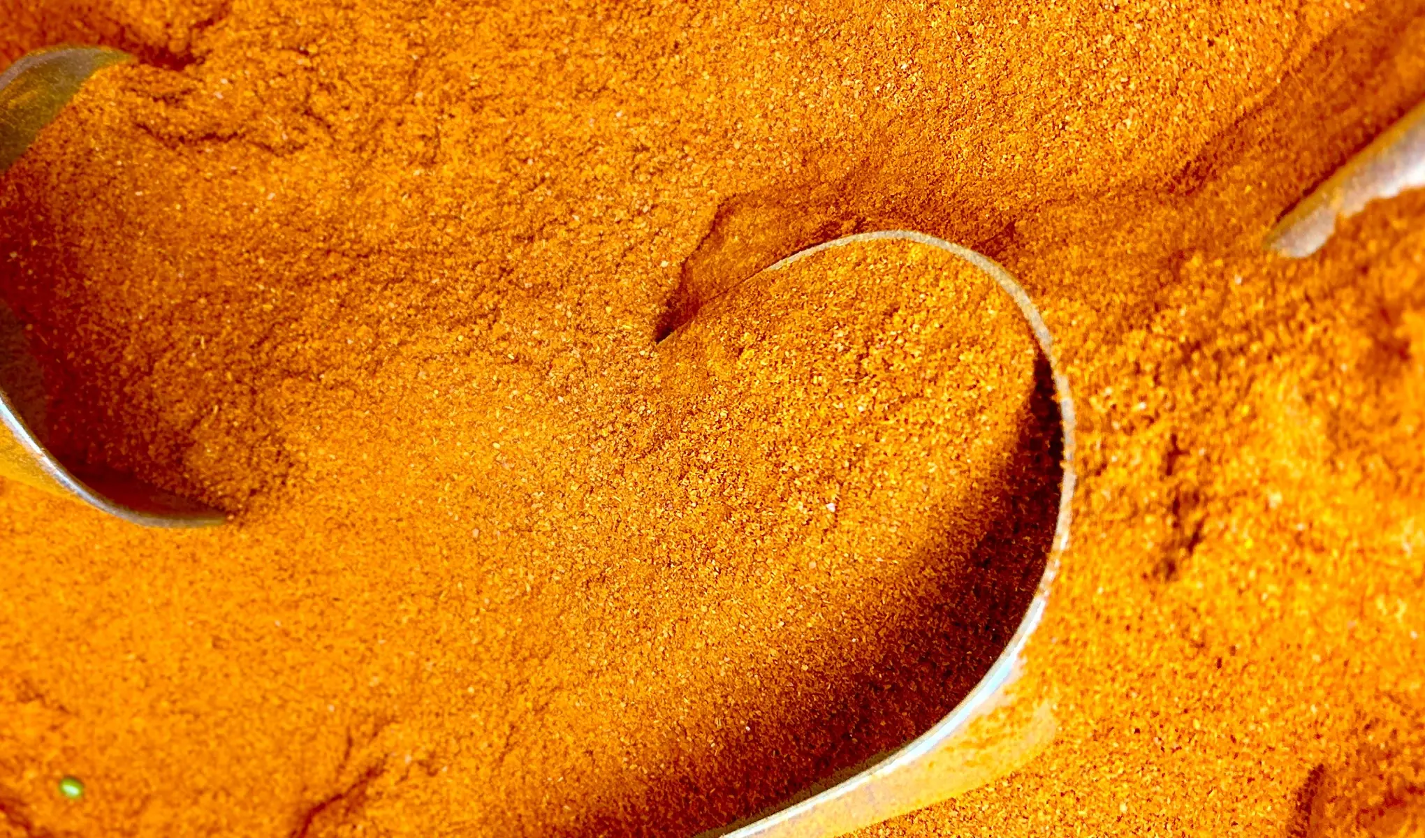 Oranssinsävyistä kurkumaa, jota nostetaan metallilusikoilla.