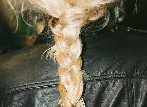 Nærbilde av en flette i lyst blondt hår over en svart skinnjakke, med fokus på hårstruktur og styling for hårpleie.