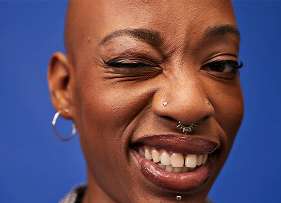Person med blå bakgrund, silverörhänge och näspiercing.