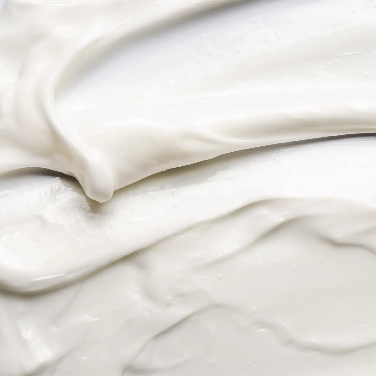 Närbild av en vit hudvårdskräm med mjuk, krämig konsistens utsmetad i böljande rörelser. Texturbild som framhäver en återfuktande ansiktskräm eller body lotion med glansig finish.