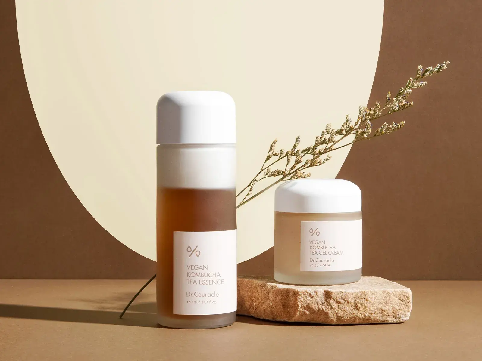 To hudpleieprodukter fra Dr.Ceuracle står plassert mot en beige og brun bakgrunn med en dekorativ plante.