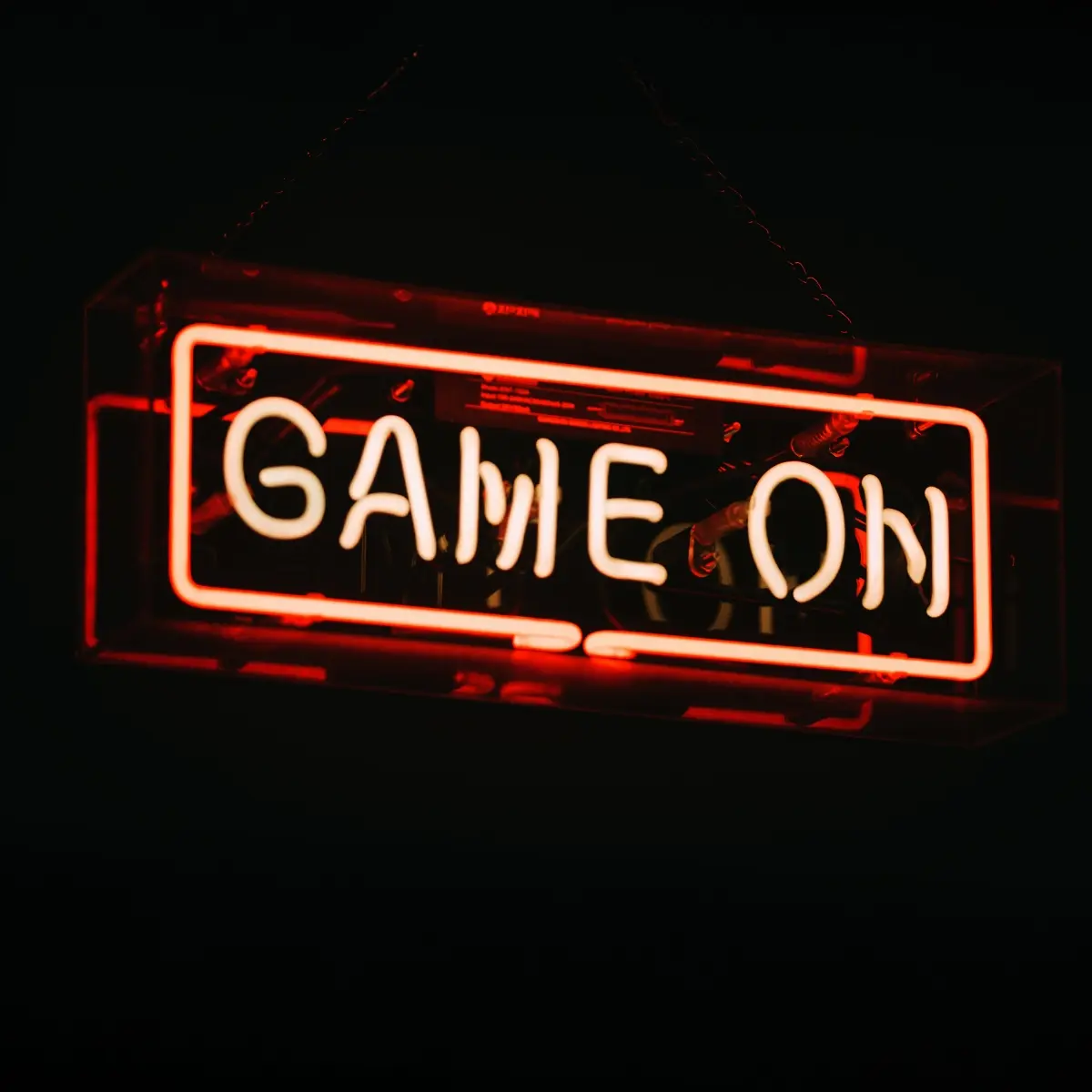 Punainen ja valkoinen neonvalo tekstillä “GAME ON” tummalla taustalla. Valaistu kyltti luo modernin ja intensiivisen gaming-tunnelman.