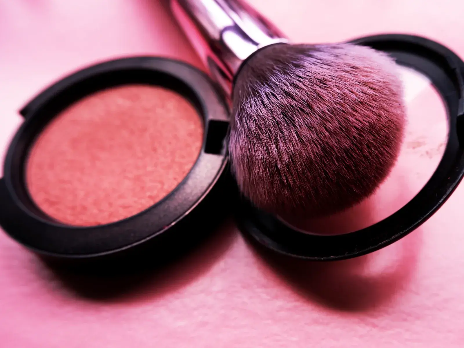 Sminkborste med rosa puder placerad i en öppen Rouge på en rosa yta