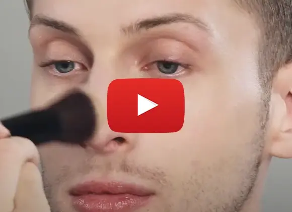 Bild på en person som för en makeup borste över näsan. Med en YouTube-spelknapp över. Översätt till norska och finska.