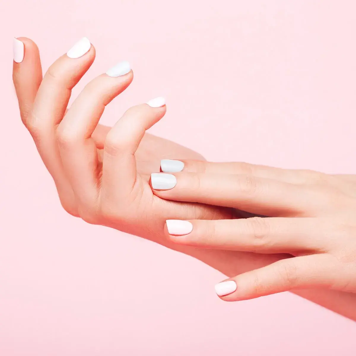 Händer med vit nagellack på rosa bakgrund.
