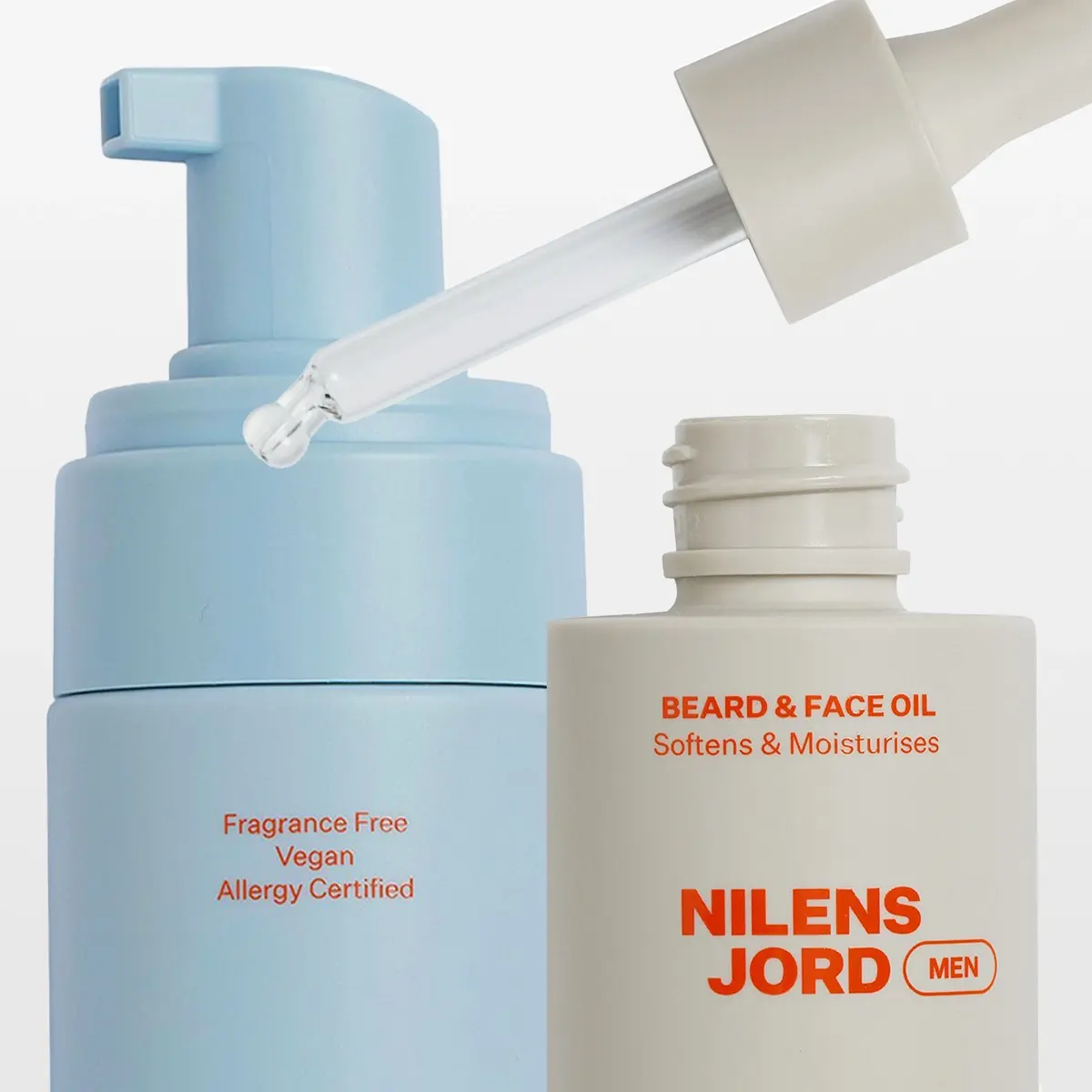 Hudvårds- och groomingprodukter från Nilens Jord MEN visas mot ljus bakgrund, inklusive skumrengöring, roll-on och Beard & Face Oil med pipett. Synlig text på förpackningarna inkluderar “Fragrance Free”, “Vegan”, “Allergy Certified”, “BEARD & FACE OIL Softens & Moisturises” och “NILENS JORD MEN”.