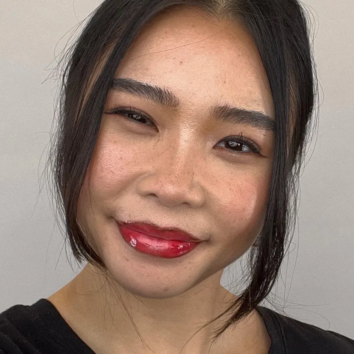 Närbild på en leende person med cherry cola-läppar – en trendig makeupstil med mörkare läppkontur och glansigt rött läppstift.