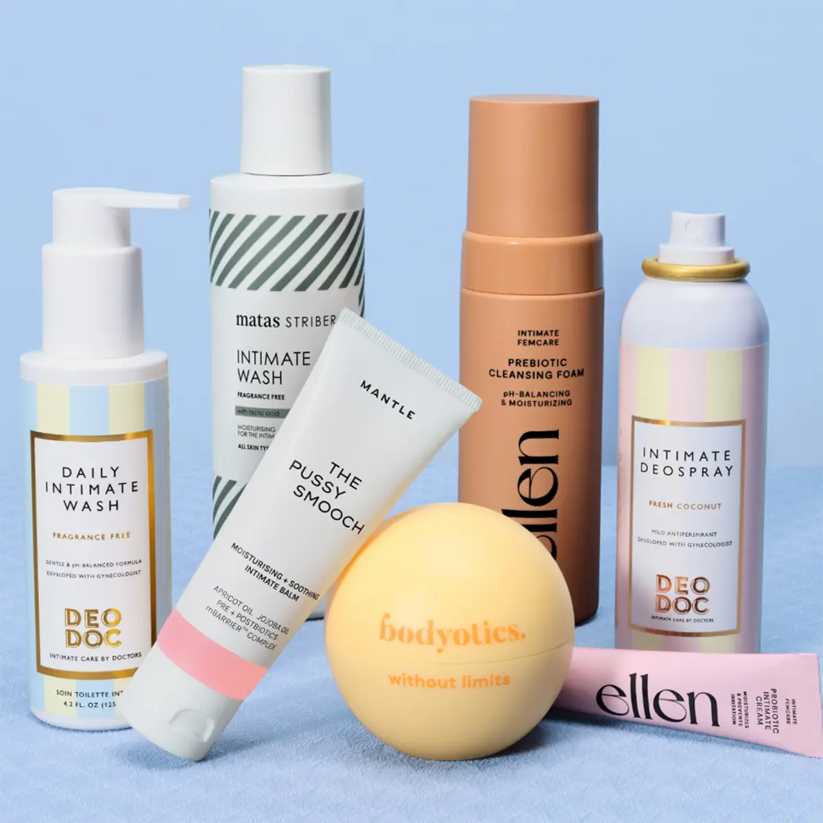 Useita intiimihygienia- ja ihonhoitotuotteita esillä vaaleansinistä taustaa vasten, mukana muun muassa DeoDoc Daily Intimate Wash Fragrance Free, Matas Striber Intimate Wash, Mantle The Pussy Smooch, ellen Prebiotic Cleansing Foam, Bodyotics without limits ja Intimate Deospray Fresh Coconut. Tuotteissa näkyy pastellisävyinen pakkausdesign sekä tekstejä intiimipesusta, prebioottisesta puhdistuksesta, deodoranttisuihkeesta ja kosteuttavasta intiimialueen hoidosta.