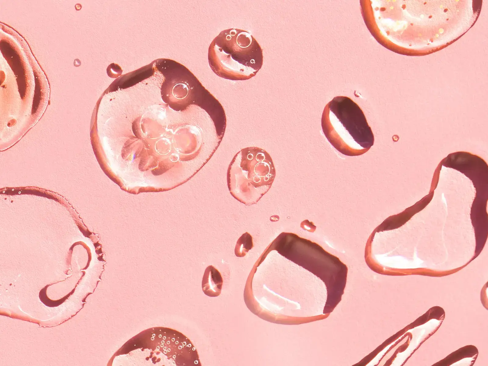Nærbilde av gjennomsiktige dråper på en rosa overflate.