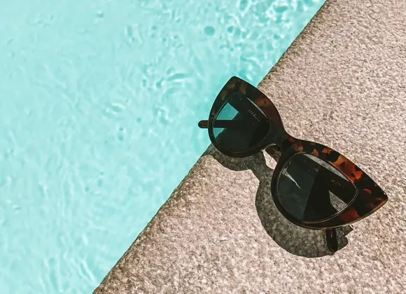 Solbriller på kanten av et svømmebasseng i solen.