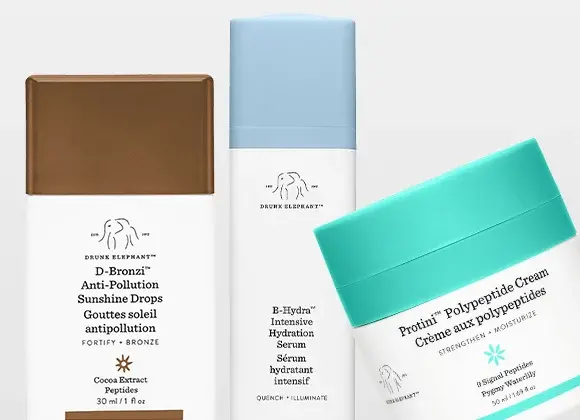 Tre hudvårdsprodukter från Drunk Elephant visas mot ljus bakgrund: D-Bronzi Anti-Pollution Sunshine Drops i brun flaska, E-Hydra Intensive Hydration Serum i vit och blå förpackning, samt Protini Polypeptide Cream i burk med turkos lock.