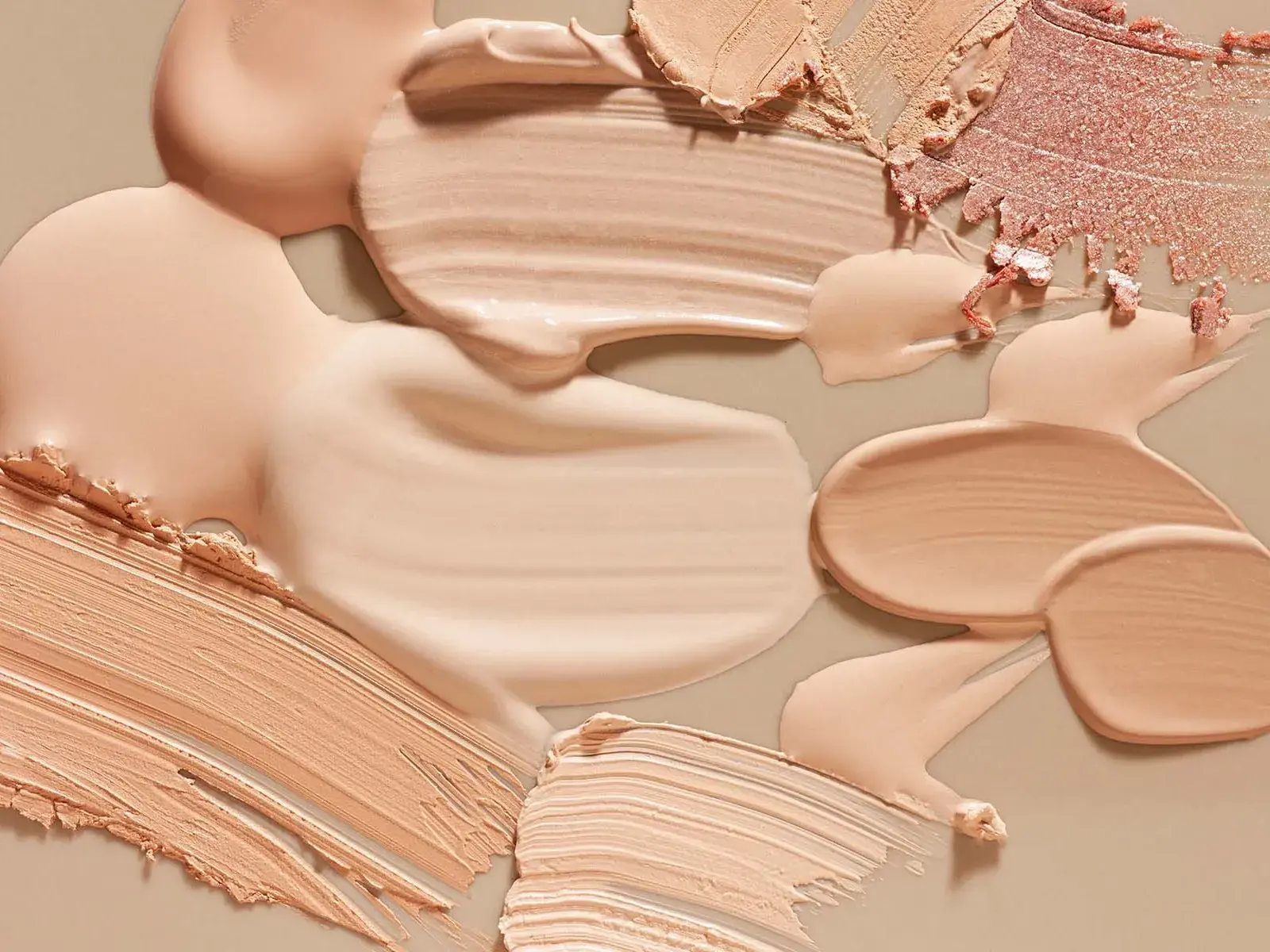 Närbild av olika nyanser av foundation och smink utsmetat på en beige yta.