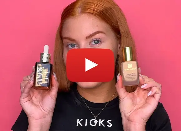 En person med rødt hår holder opp to Estée Lauder-produkter, Advanced Night Repair og Double Wear foundation, foran en rosa bakgrunn.