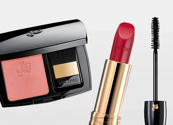 Lancôme-meikkiä: vaaleanpunainen poskipuna mustassa rasiassa peilillä ja siveltimellä, punainen huulipuna kullanvärisessä hylsyssä sekä ripsiväri harjalla. Lancôme-brändin nimi näkyy meikkituotteiden pakkauksissa: poskipuna, huulipuna ja mascara.