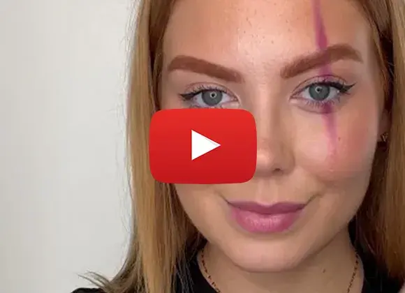 Närbild på en ung kvinna med långt rödblont hår och smink, med ett vertikalt streck av rosa färg över ena ögat. En YouTube-spelikon är överlagrad på bilden.