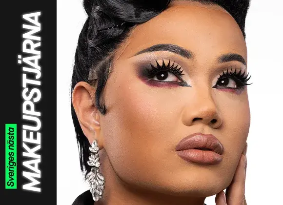 En person med en elegant makeuplook som kombinerar markerad ögonmakeup i guld, svart och vinrött med långa fransar, skulpterad bas och neutrala läppar, kompletterat med stora glittrande örhängen och en uppsatt frisyr.