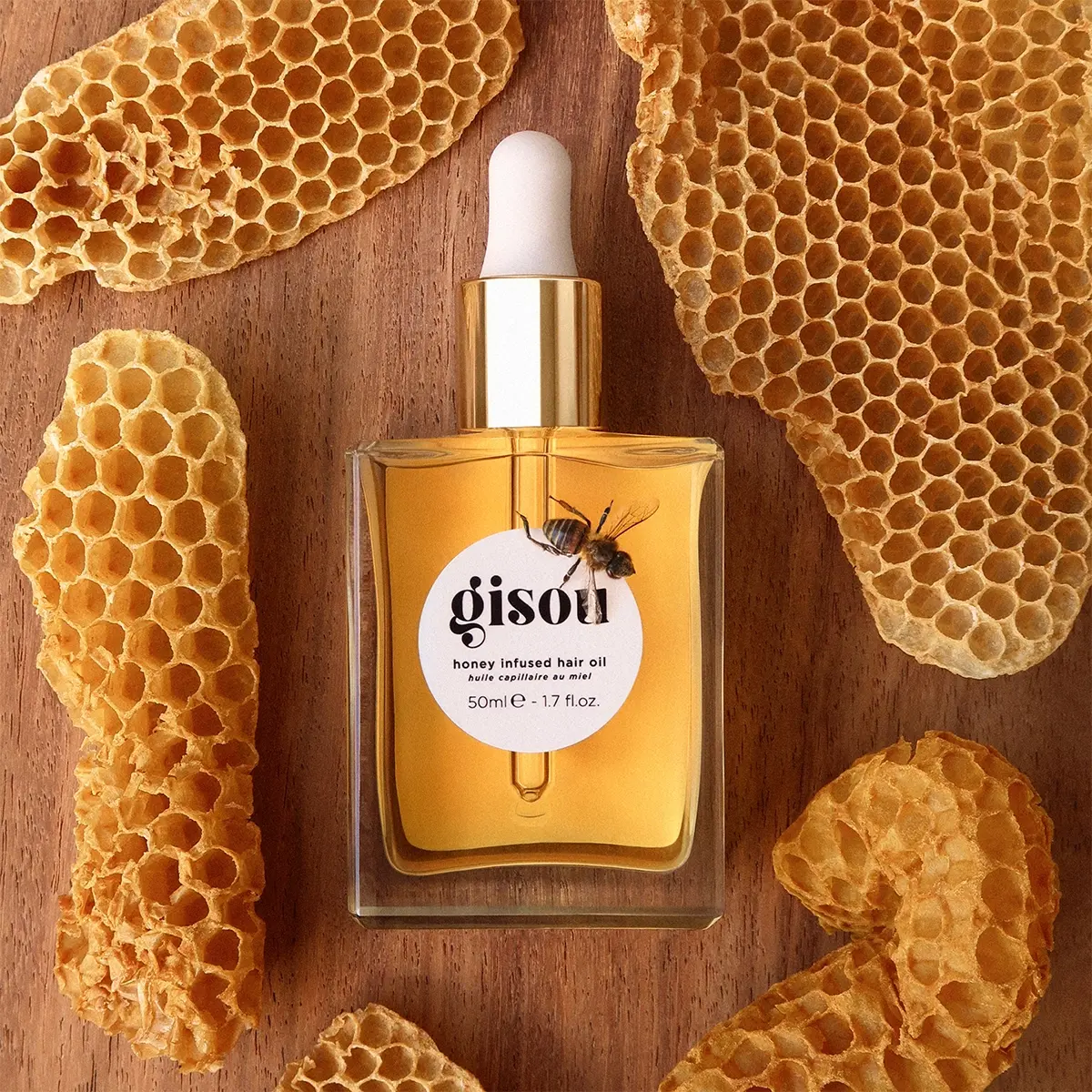 Gisou Honey Infused Hair Oil-flaske med honningkake og bie. Tekst: Gisou Honey Infused Hair Oil, huile capillaire miel, 50ml e 1.7 fl.oz.