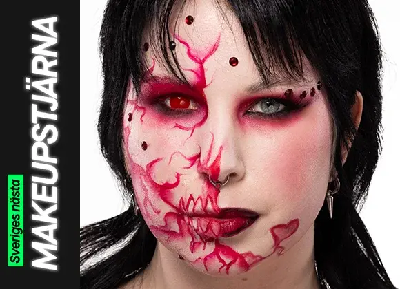 Porträtt av en person med svart hår och kreativ makeup där ansiktet är målat med röda linjer, mönster och dekorativa detaljer, fotograferad mot ljus bakgrund.