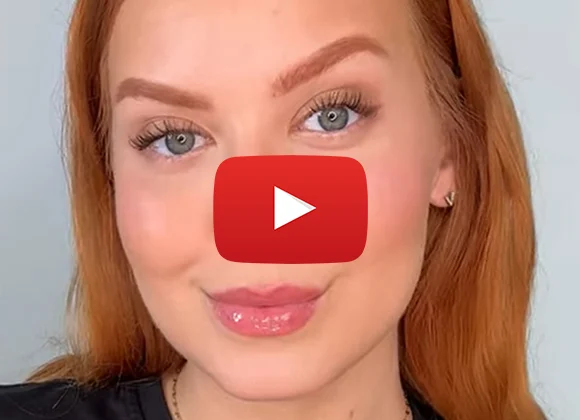 En person med långt rött hår bär en svart tröja och ett guldhalsband. Framför henne finns en röd YouTube-knapp.