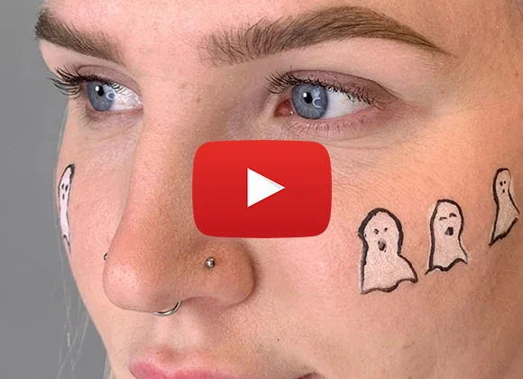 Närbild på en person som hafr tre vita spöken ritat på kinden. Personen har en piercing i näsan. Det är en youtube play symbol i mitten av bilden.