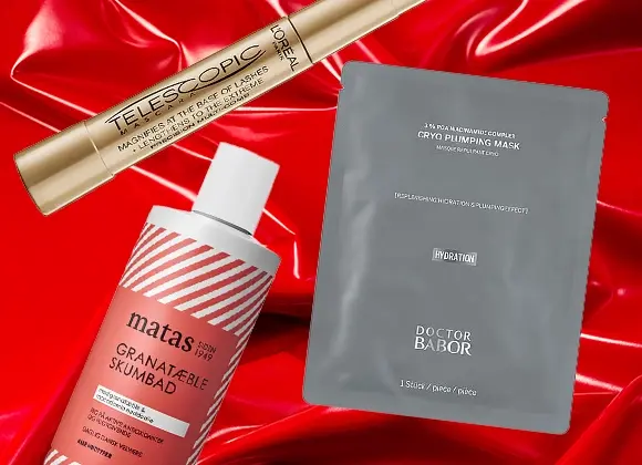 Tre skönhetsprodukter mot en röd, glansig bakgrund: en guldmaskara från L’Oréal Paris, en grå ansiktsmask från Doctor Babor och ett rött skumbad från Matas med granatäpple. Perfekta prisvärda julklappstips inom skönhet och hudvård.