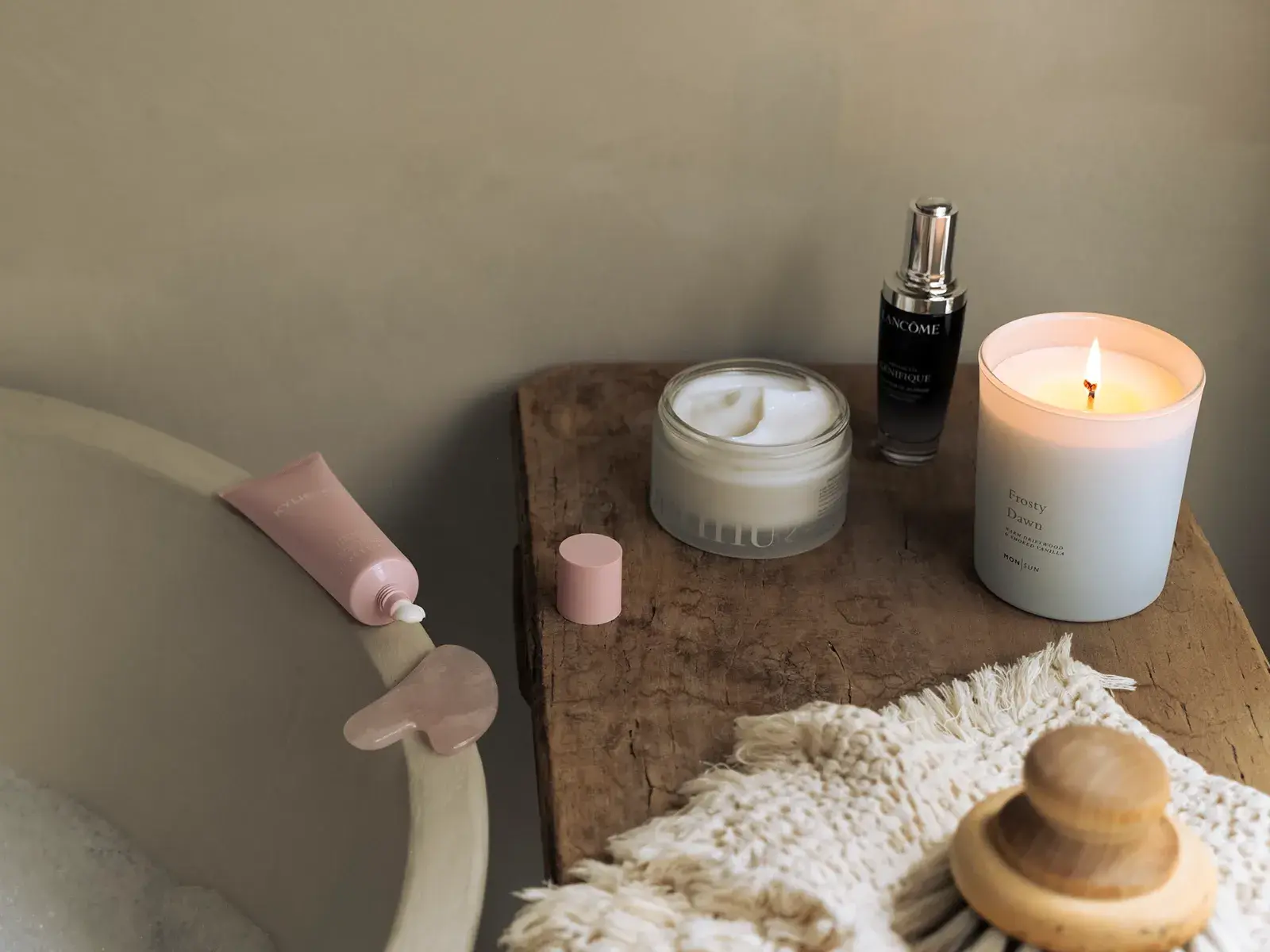 Hemmaspa-miljö med badkar, hudvårdsprodukter, tänd doftljus och en gua sha-sten på ett träbord.