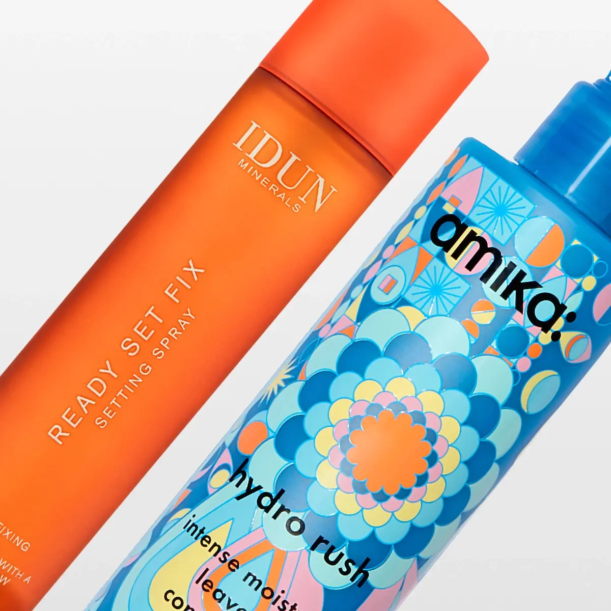 Oranssi IDUN Minerals Ready Set Fix -kiinnityssuihke ja sininen Amika Hydro Rush Intense Moisture Leave-in -pullo.