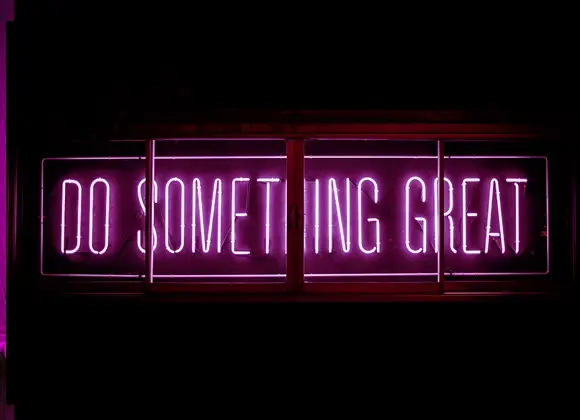 Rosa neonskylt med texten "Do something great"mot mörk bakgrund.