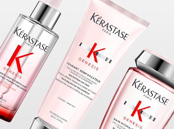 Produktbild med tre hårvårdsprodukter från Kérastase Paris Genesis-serie mot en ljus bakgrund. Synliga produkter är ett serum, ett balsam och ett schampo i rosa och silvertoner. Perfekt för stärkande och vårdande hårvård.