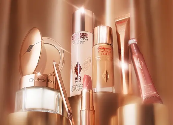 En samling av Charlotte Tilbury beautyprodukter, inklusive Airbrush Flawless Setting Spray, Hollywood Flawless Filter, Hollywood Contour Wand, Glowgasm Beauty Light Wand, en läppenna och ett puderkompakt. Produkterna är elegant placerade och belysta med ett varmt sken.