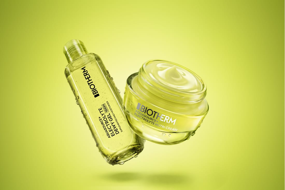 Biotherm Aquasource hudvård med Aquasource Electrolyte Gel och Aquasource Electrolyte Nutri Cream svävar mot en limegrön bakgrund med vattendroppar på förpackningarna. Texterna "BIOTHERM", "AQUASOURCE ELECTROLYTE GEL", "AQUASOURCE ELECTROLYTE NUTRI CREAM" och "SUITABLE FOR ALL SKIN TYPES" syns på produkterna.