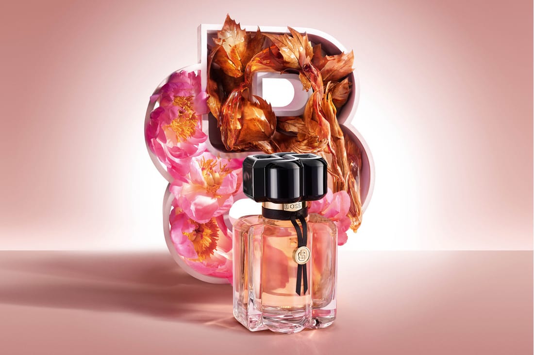 BOSS-parfyme mot rosa bakgrunn med blomster og ravfargede blader.