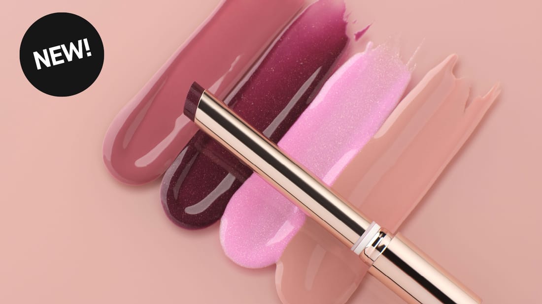 Anastasia Beverly Hills Kiss Theory Lip Balm och glansiga läppfärger mot rosa bakgrund. Text: ”NEW!”