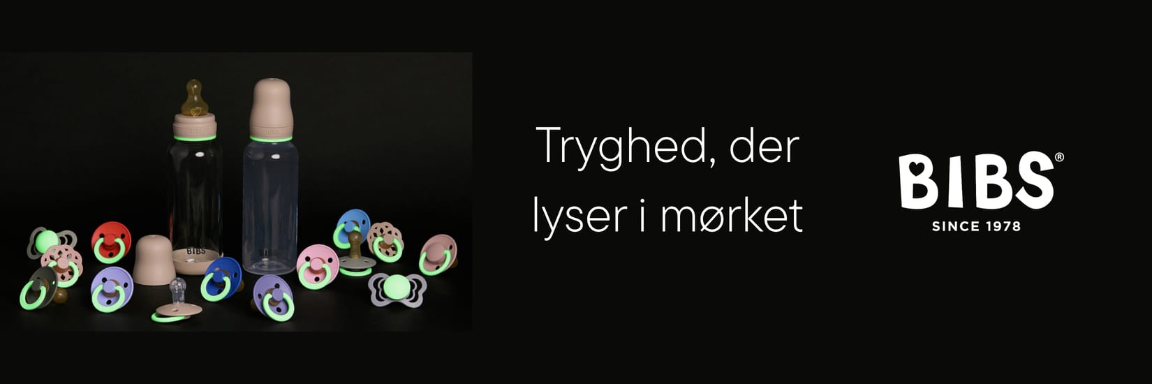 BIBS sutteflasker og sutter med selvlysende detaljer på sort baggrund. Tekst: “Tryghed, der lyser i mørket” samt BIBS-logo.