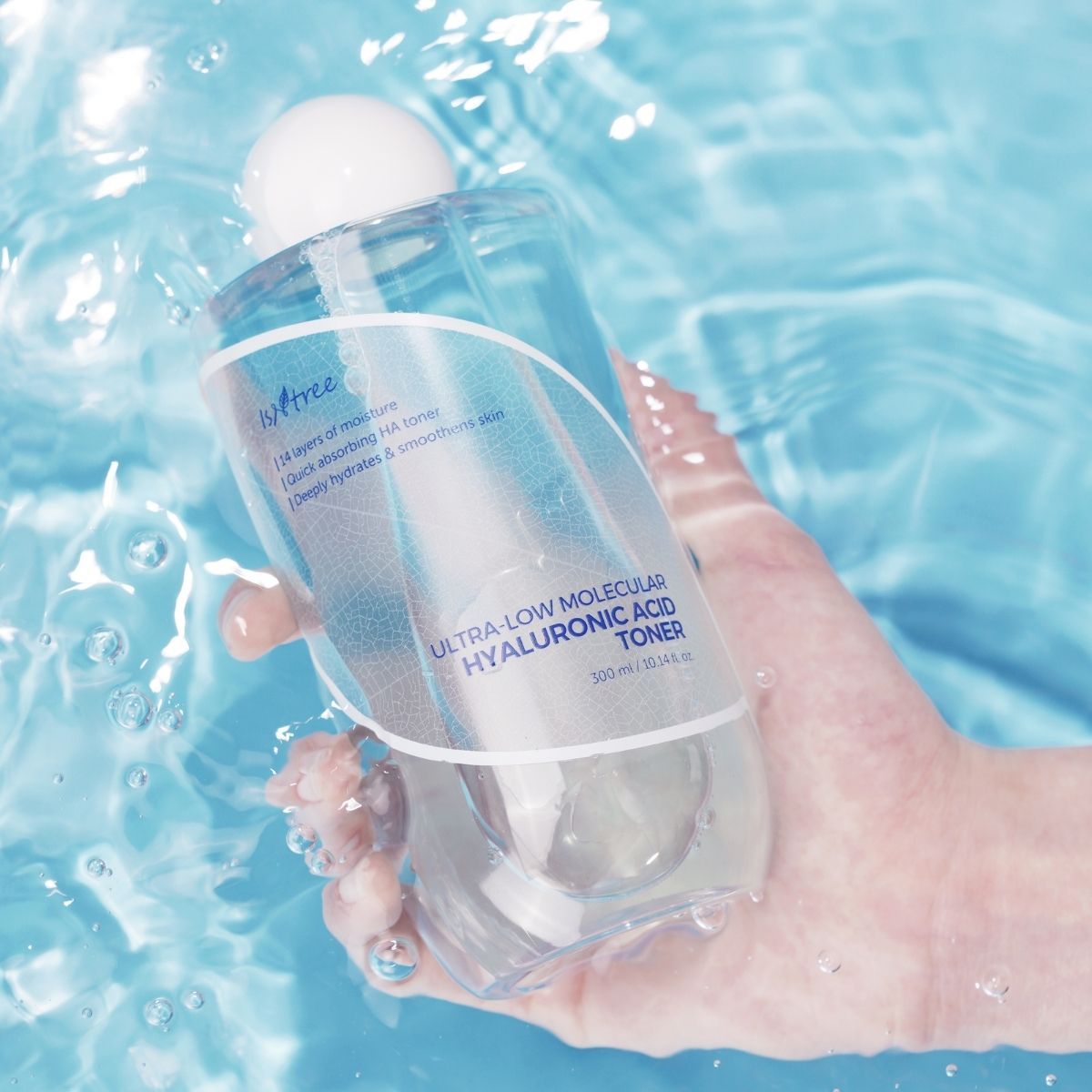 En hånd holder en flaske Isntree Ultra-Low Molecular Hyaluronic Acid Toner delvist nedsænket i klart, blåt vand.