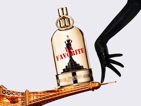 Her ses Jean Paul Gaultier La Favorite i en guldfarvet parfumeflakon med teksten “La Favorite”. Flakonen balancerer på en guldfarvet Eiffeltårn-figur, mens en sort handskeklædt hånd ses til højre.