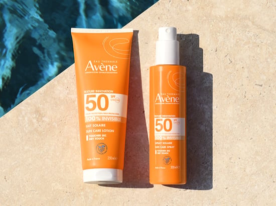 Her ses Avène solprodukter med SPF 50 på en stenoverflade ved vand.