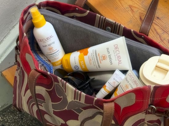 Her ses Decubal solprodukter placeret i en åben strandtaske sammen med solbriller og en drikkedunk.