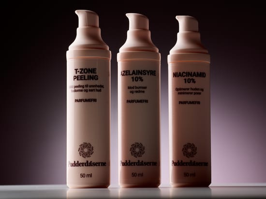 Her ses tre hudplejeprodukter fra Pudderdåserne: T-Zone Peeling, Azelainsyre 10% og Niacinamid 10%. Produkterne står i lyserøde pumpeflasker mod en mørk baggrund. På emballagerne fremhæves produkternes egenskaber, og alle tre er markeret som parfumefri.