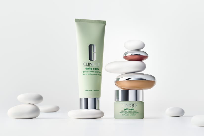 Clinique Daily Calm-rengöringskräm och ansiktskräm omgivna av vita stenar mot ljus bakgrund.