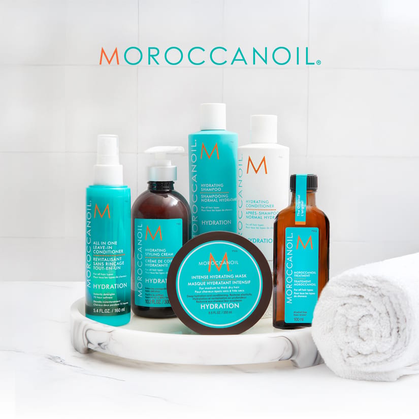 Her ses seks Moroccanoil Hydration-hårplejeprodukter på et marmorfad med et hvidt håndklæde. Tekst på billedet: “MOROCCANOIL”.