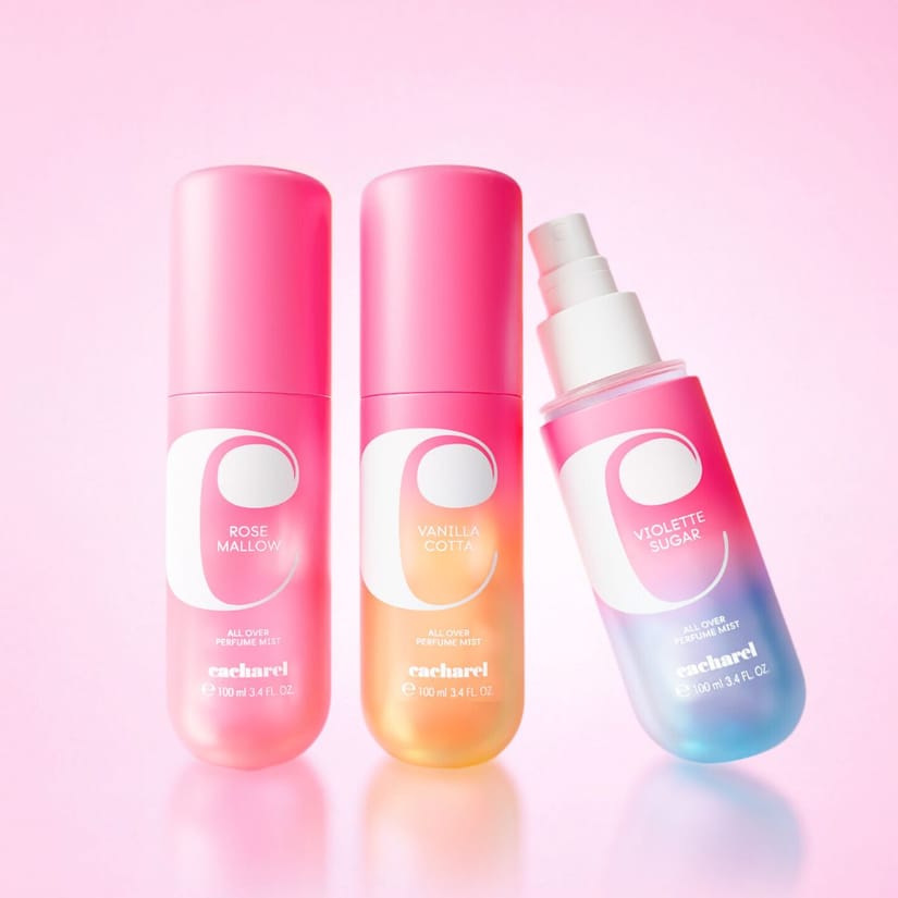 Her ses tre Cacharel All Over Perfume Mist i pink, orange og blå emballage på en lyserød baggrund.